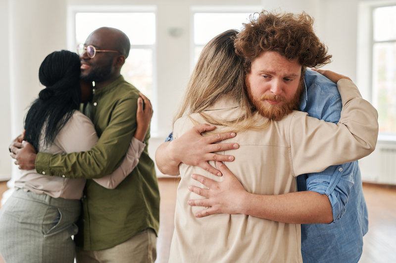 Young man giving hug to female against African American patients standing in embrace while attending course of psychological help