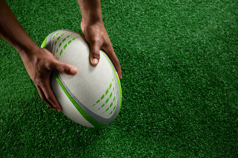 High angle view of hands holding rugby ball on field