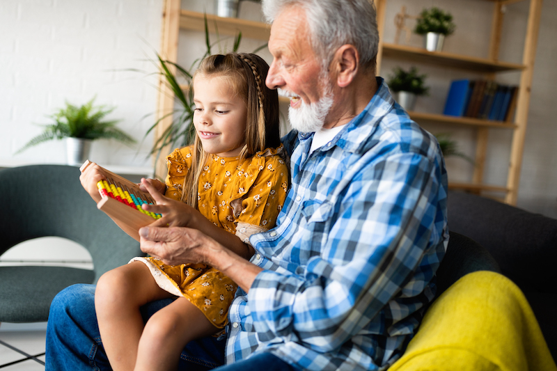 Handsome grandfather and grandchild are talking and smiling while playing with toys together at home