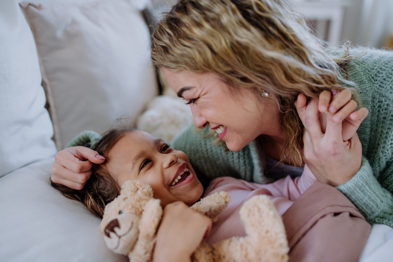 A happy mother stroking her little daughter when waking her up in morning.