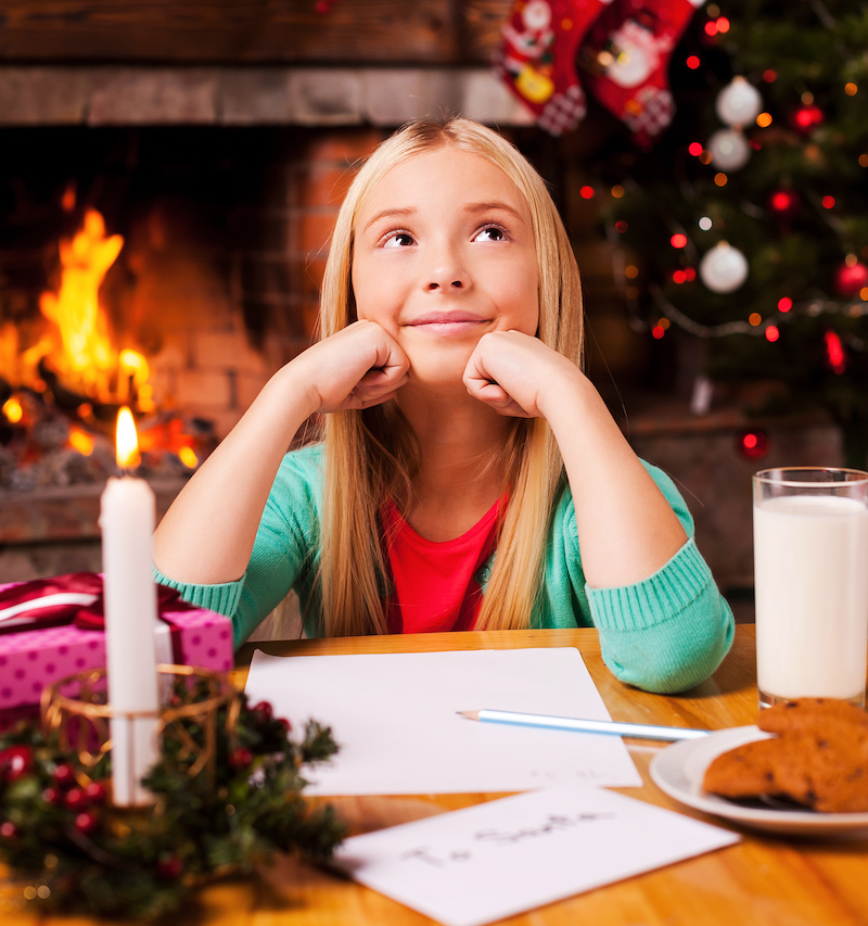 What do I wish? Cute little girl day dreaming while sitting at home with Christmas tree and fireplace in the background