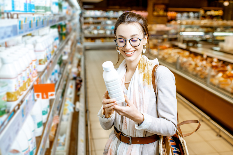 Young woman choosing milk standing near the shelves with dairy products in the supermarket