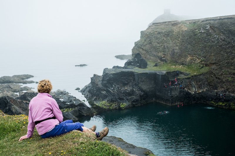 Woman sitting on top of a cliff on the Pembrokeshire Coast, Wales, UK.