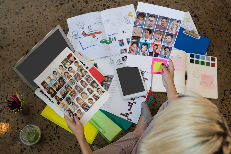 High angle view of young Caucasian businesswoman holding documents sitting on floor at creative office