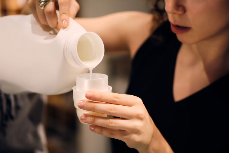 Close up girl holding detergent bottle washing clothes in self-service laundry