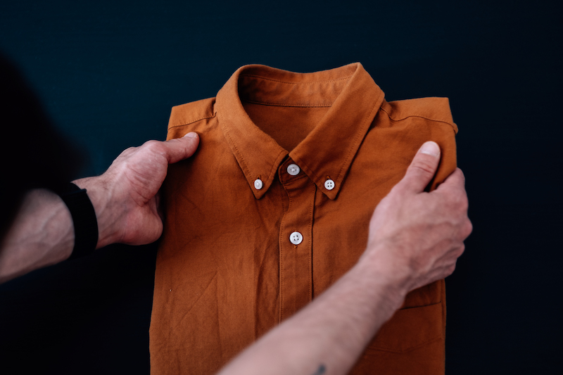 A male folding an orange shirt on the table