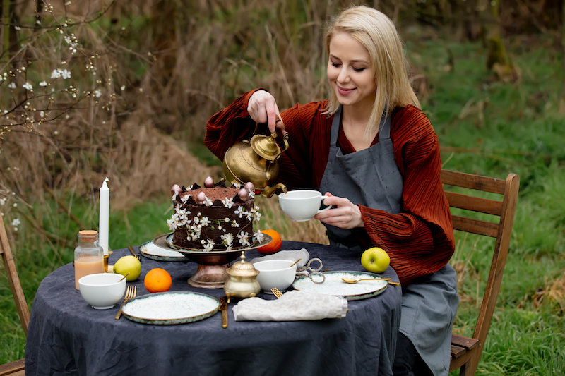 woman pours tea into a cup in the garden near the cherries garden