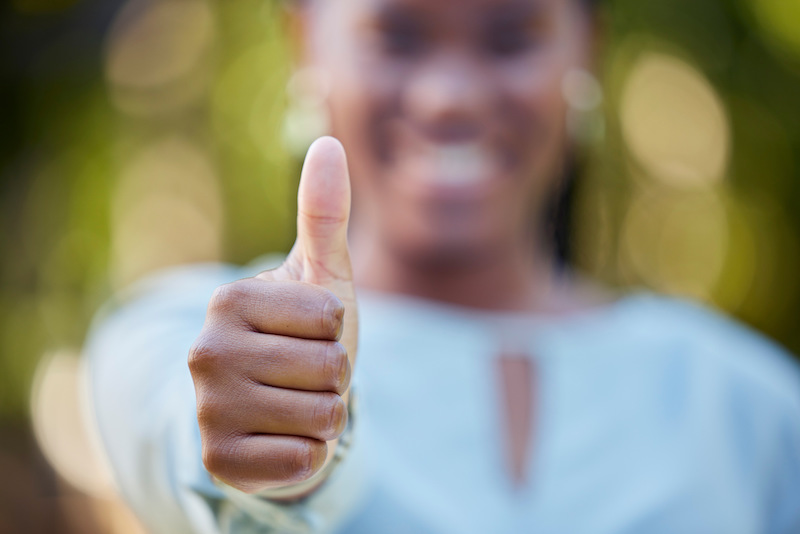 Hand, closeup and thumbs up by black woman showing yes, recommendation or thank you on bokeh backgr.