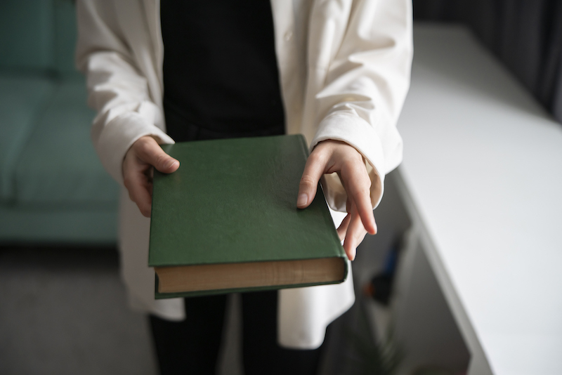 Close-Up of a Person's Hands Offering a Green hardcover Book Indoors