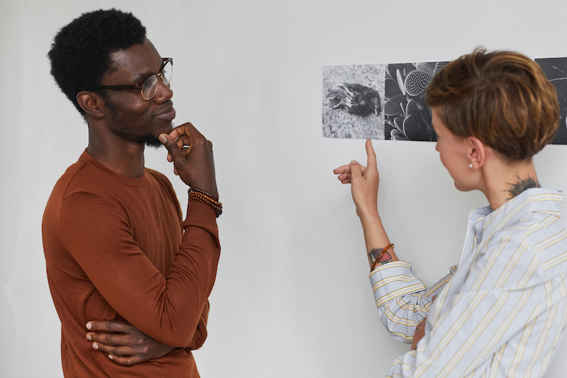 Waist up portrait of two young people discussing art while exploring modern gallery exhibition