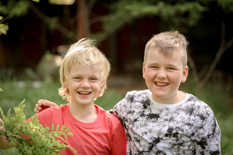 A portrait of two blonde brothers smiling widely at the camera