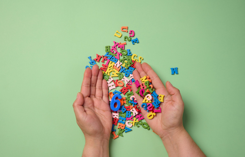 Two female hands and scattered wooden letters of the English alphabet on a green background