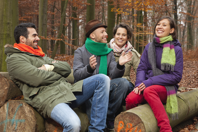 Germany, Berlin, Wandlitz, Men and women sitting on tree trunk, smiling