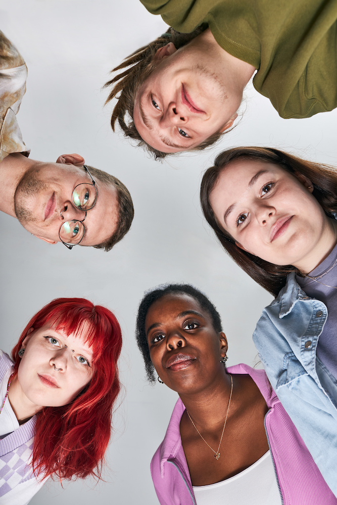 Portrait of diverse group of young adults looking up towards camera smiling in casual clothing against light background creating an inclusive and friendly image