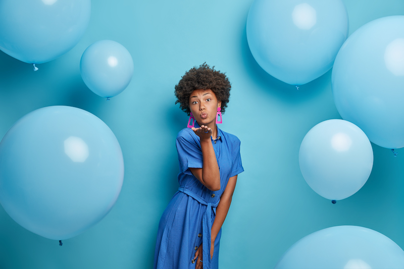 a lady dressed in blue against a blue background with balloons