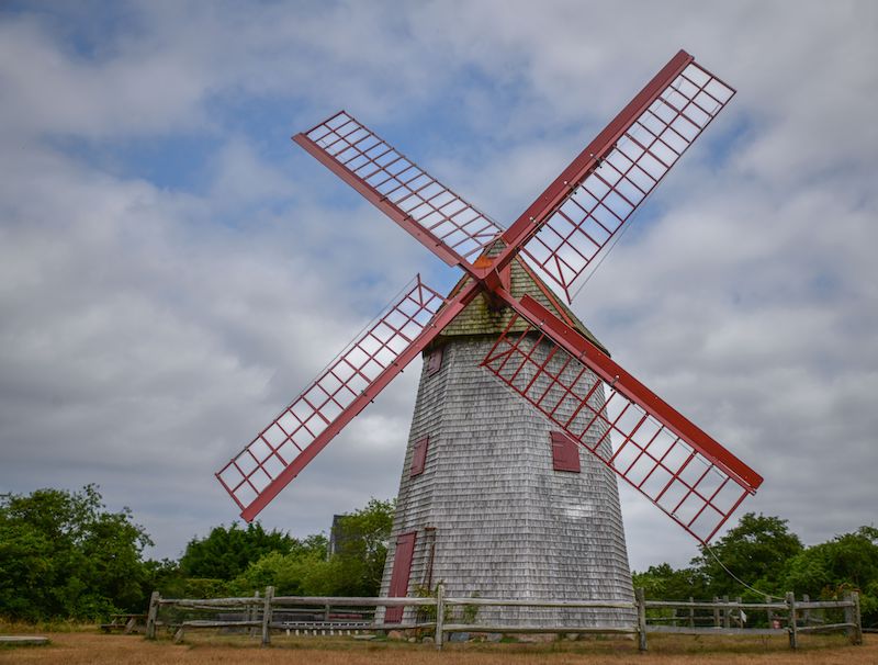 A scenic view of an old windmill in a green field on a cloudy day