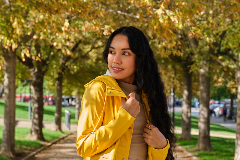 Young latin girl dressed in yellow raincoat smiling at street in autumn.