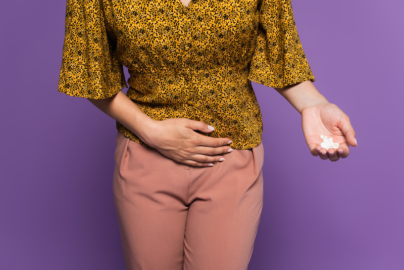 cropped view of woman with stomach ache holding pills isolated on purple