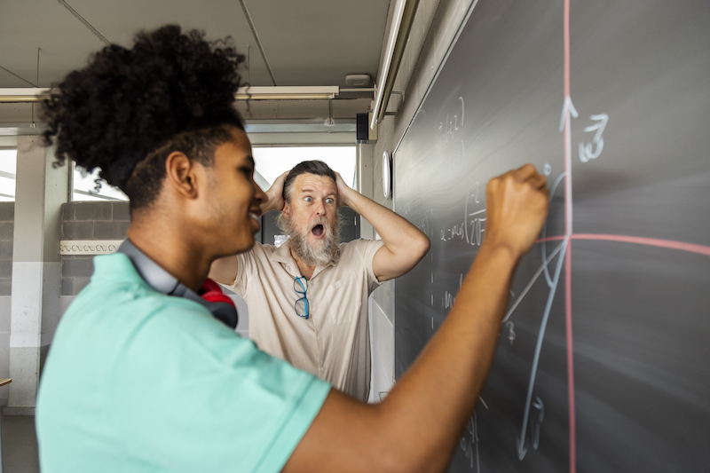 Surprised mature caucasian male teacher with how well his teen high school students solves math exercise on blackboard. 