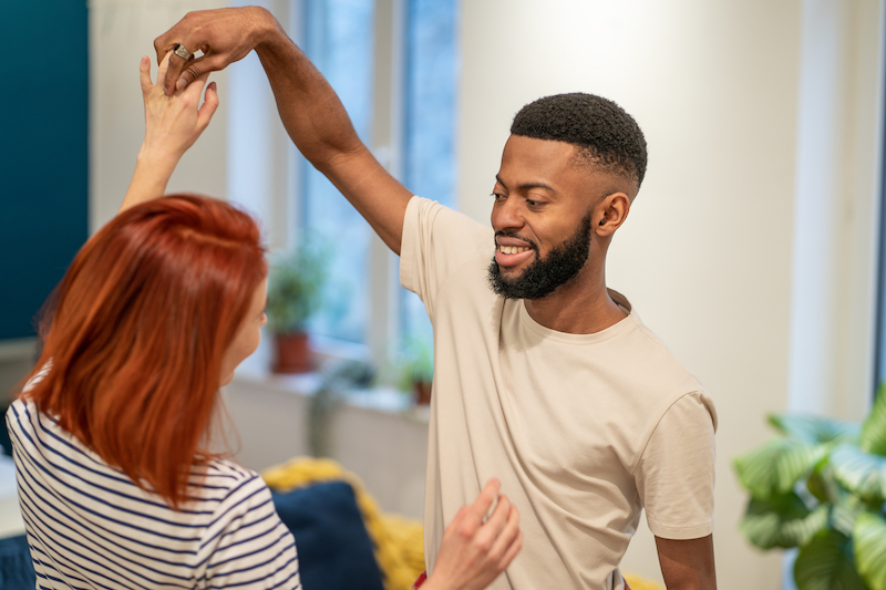 Happy romantic multiracial young couple in love holding hands enjoying dancing together