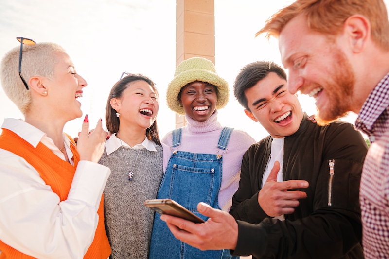 Group of young people enjoying and having fun using a cellphone and watching funny messages outside