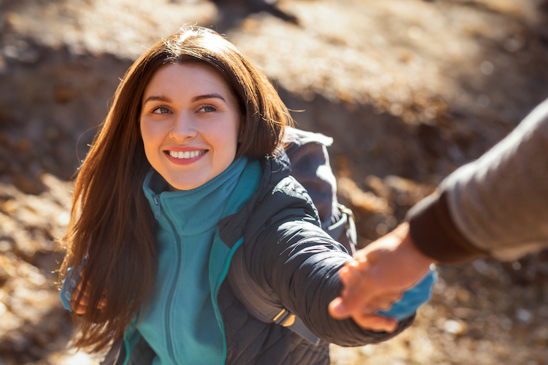 Portrait of happy young woman outstretching hand to man while hiking at forest