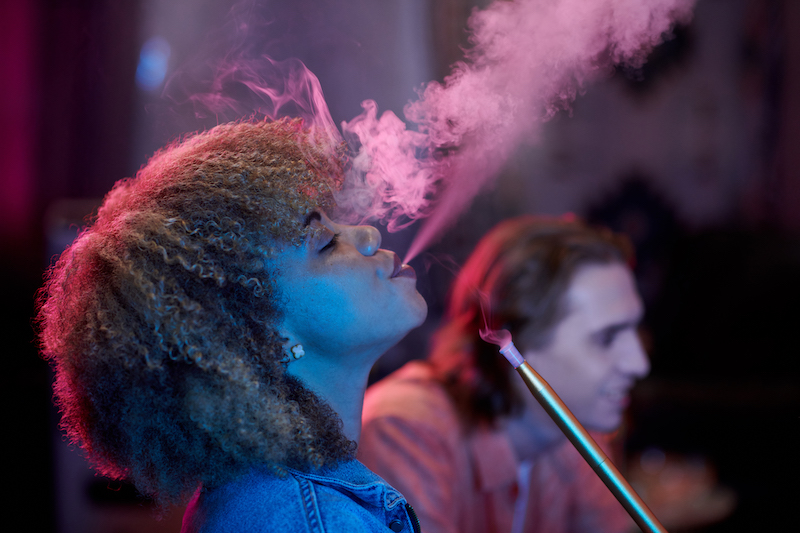 Side view of curly young woman exhaling smoke