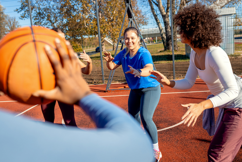 Diverse group of young woman having fun playing recreational basketball outdoors.