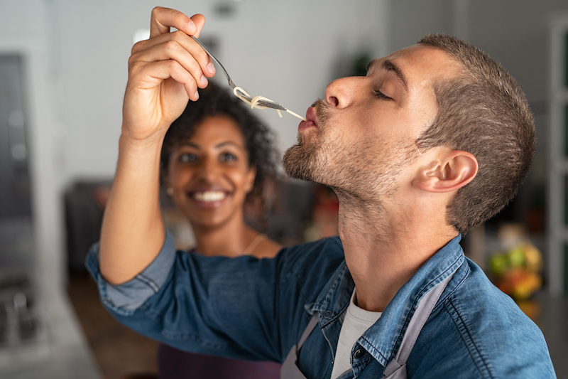 Man tasting spaghetti pasta while smiling woman look at him.