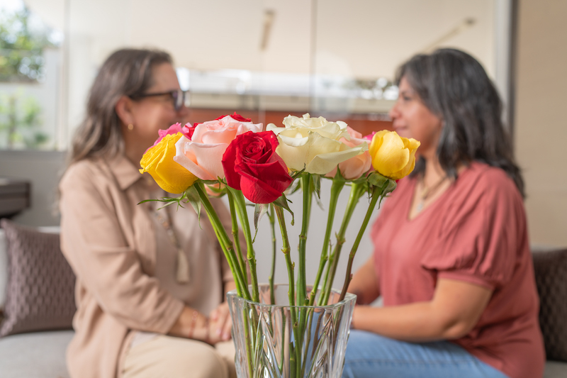 Friends sitting behind a bouquet of roses, talking