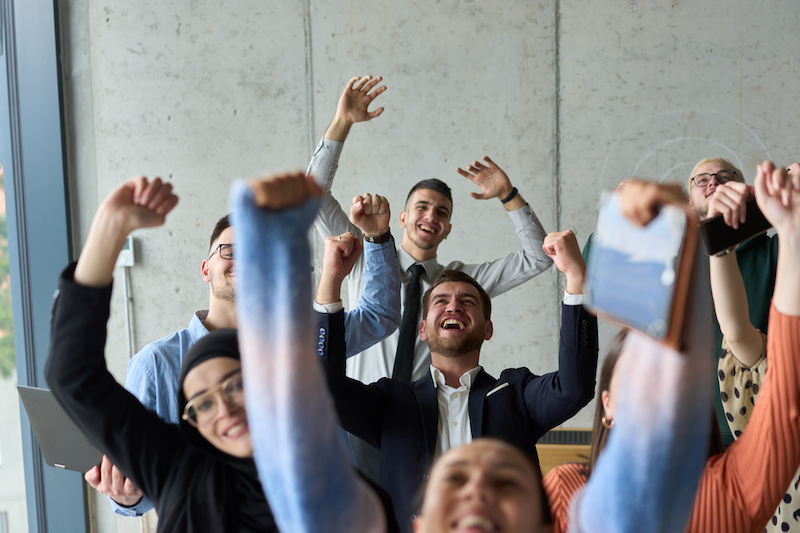 A diverse team of business professionals ecstatically celebrating their success in a modern office, expressing triumph and unity after achieving their goals.