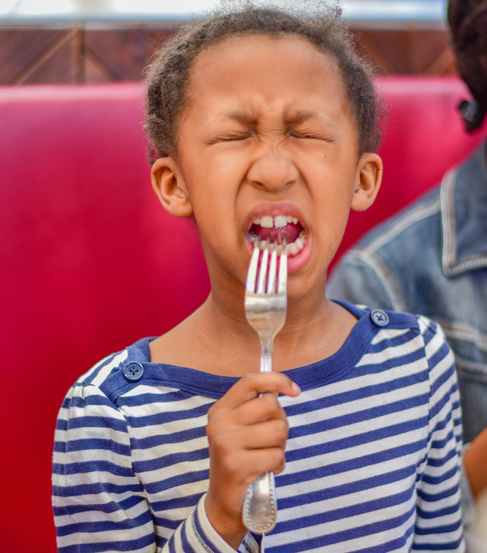 little girl making a funny face , squinting eyes, and mouth open after tasting something sour