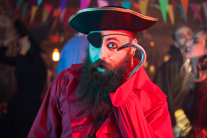 Portrait of funny man in a pirate costume playing with his hand hook at halloween celebration.