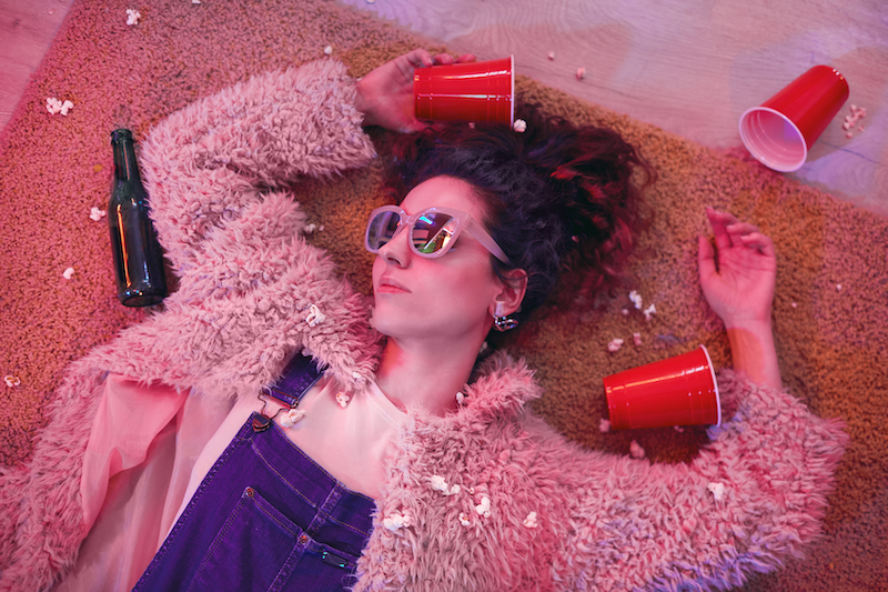 Young woman in sunglasses sleeping on the floor among empty glasses and bottles after party